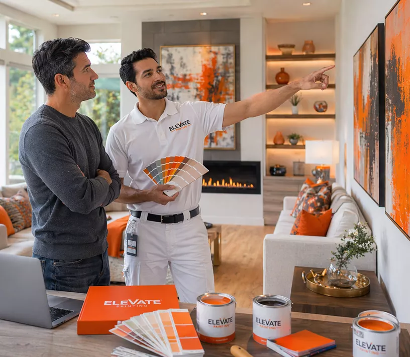 A painter holding colour swatches consults with a homeowner in a bright living room, with open paint tins and sample cards on the table