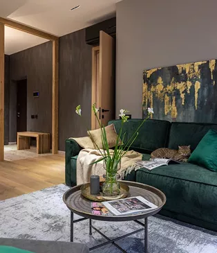 Moody living room with a dark green velvet sofa, gold abstract wall art, a round metal coffee table, and a cat resting on the cushions.