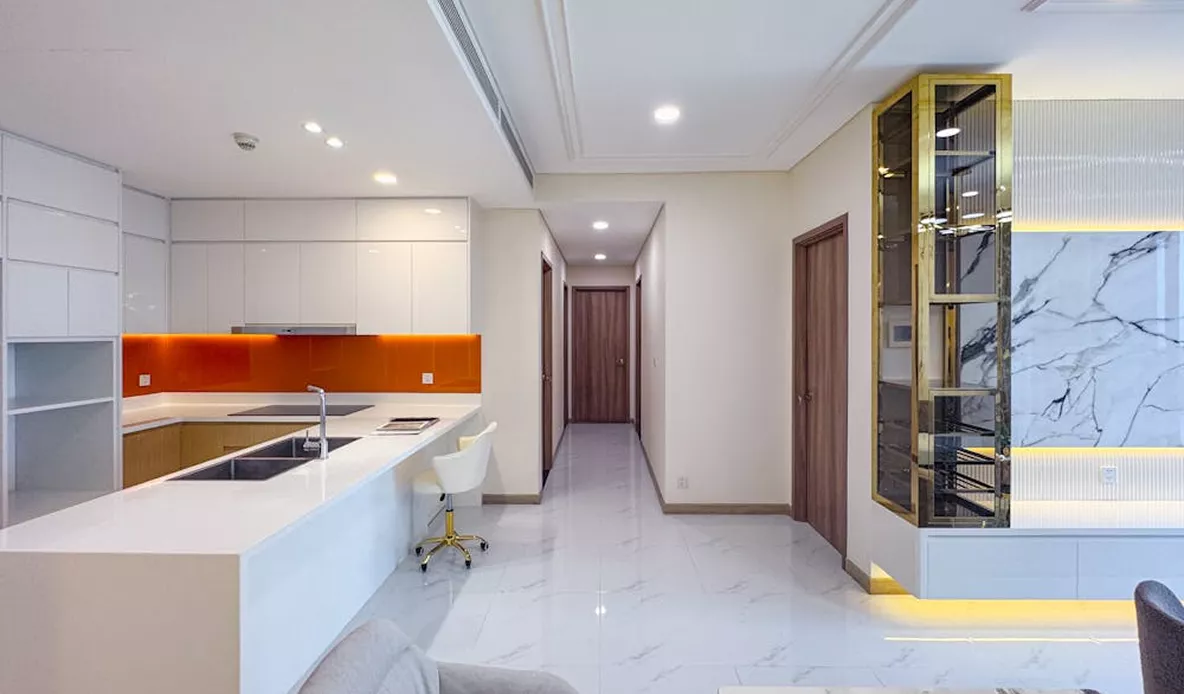Modern open-plan kitchen with white gloss cabinets, an orange glass splashback, marble floors, and a gold display cabinet unit.