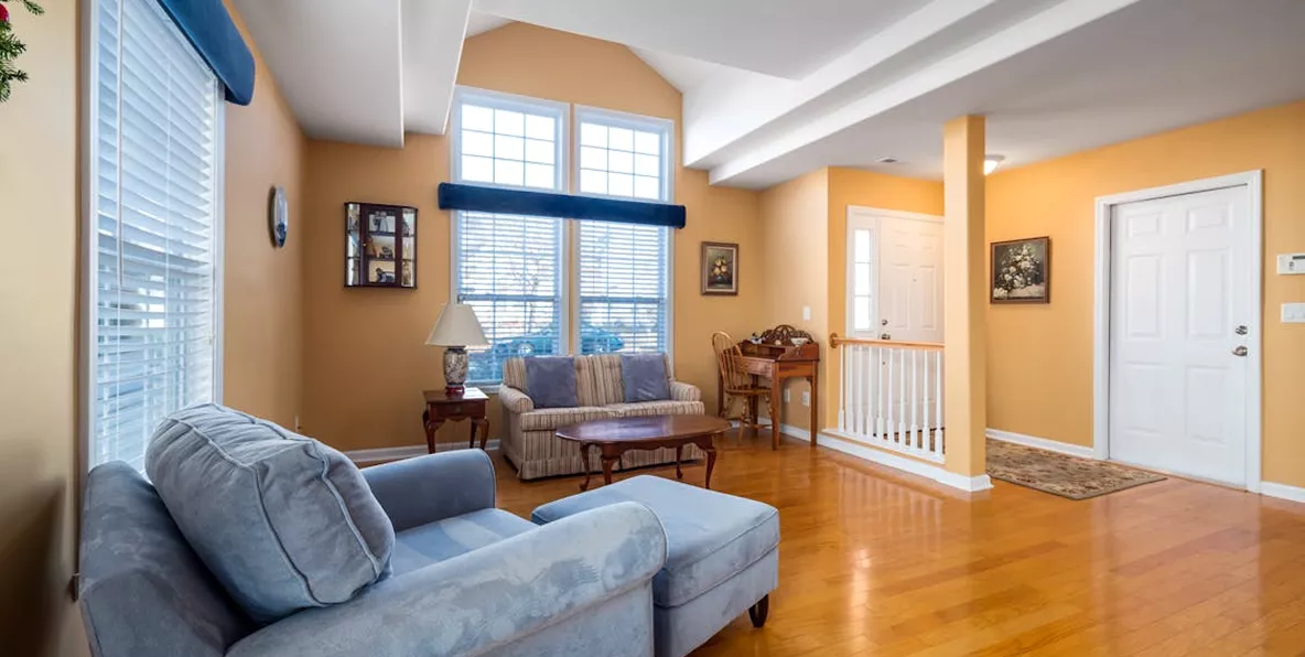 Warm living room with golden yellow walls, blue sofas, hardwood floors, vaulted ceiling, and a staircase landing visible beyond.