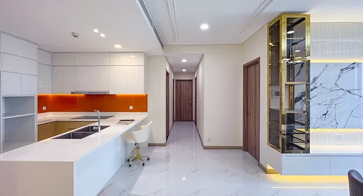 Modern minimalist kitchen with white cabinets, orange backsplash, marble floors, hallway, wooden doors, and a glass display cabinet with gold accents and lighting.