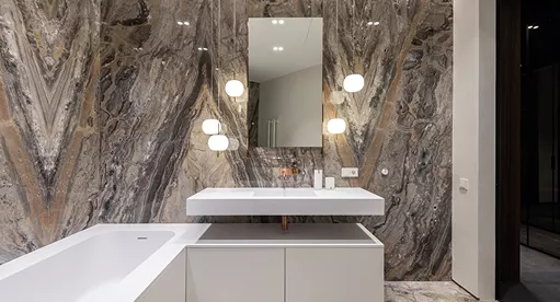 Luxury bathroom with dramatic veined marble feature walls, a freestanding white tub, floating vanity, and globe wall lights
