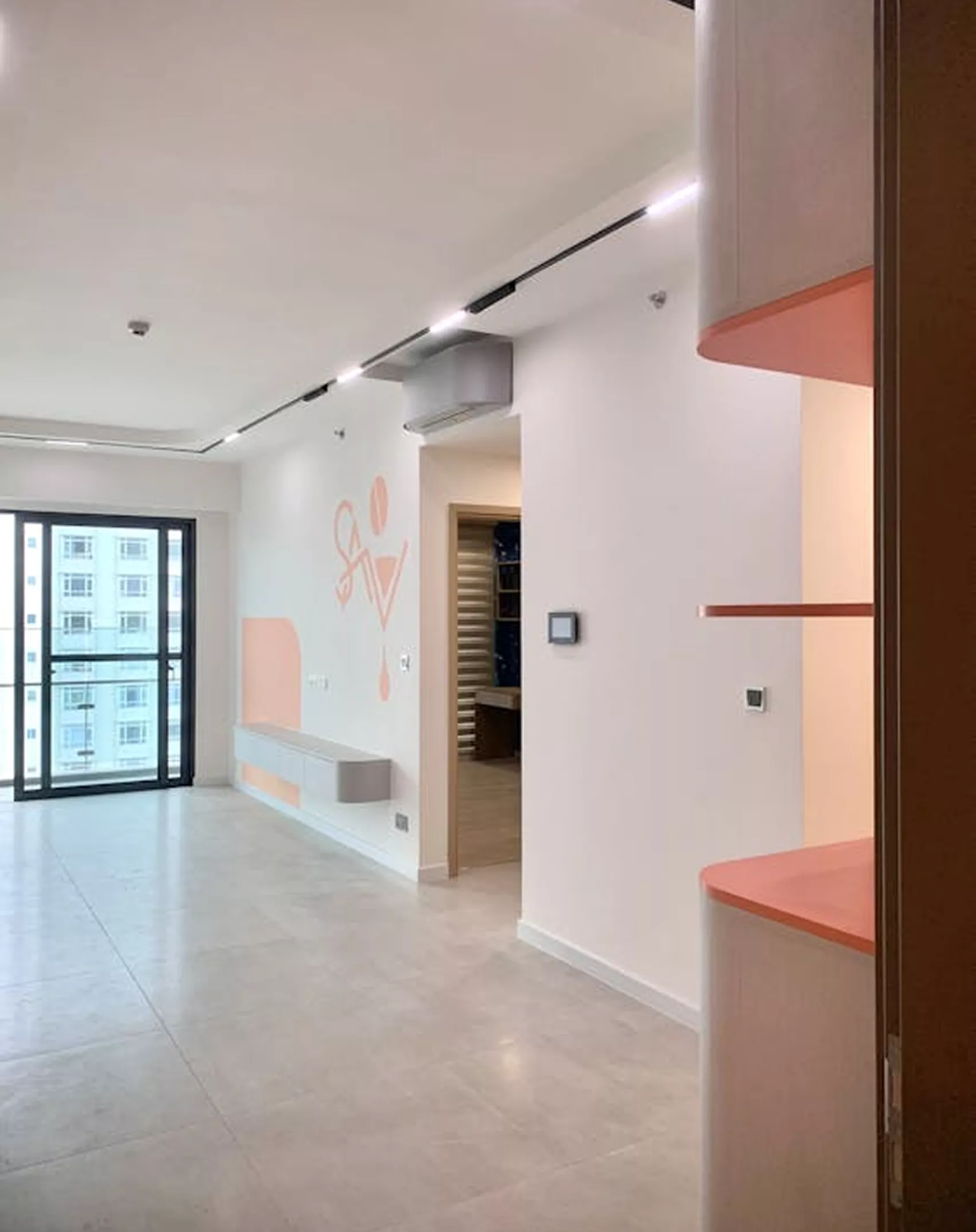Modern apartment interior with white walls featuring a coral abstract mural, track lighting, and pink-accented shelving details.